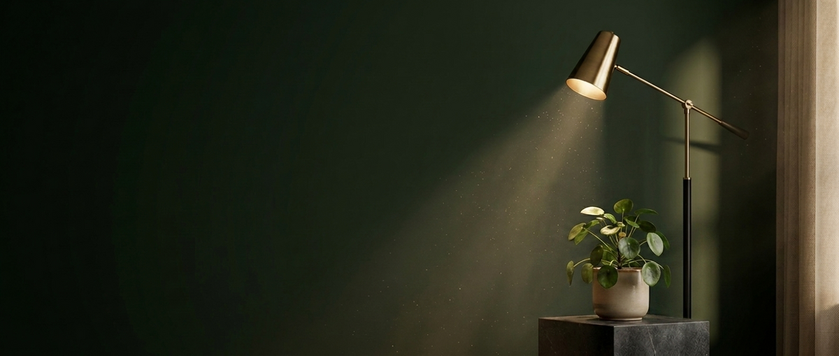 Brass task lamp casting warm light over a trailing plant against a deep green wall